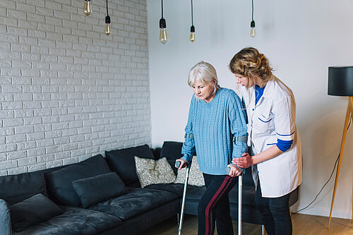 Carer helping older person on crutches
