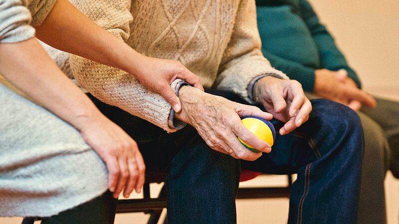 Older person holding a ball with carer supporting them
